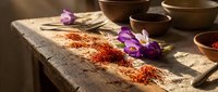 Aromatic spices scattered on rustic wooden table with purple flowers and clay bowls creating warm culinary scene for cooking and food preparation.