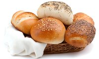 Fresh baked bread rolls with various toppings including sesame seeds and poppy seeds arranged in woven basket with white napkin, appetizing bakery food photography.