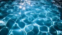 Luminous aqua blue water surface with rippling light reflections creating abstract patterns. Sunlight dancing on swimming pool waves forms mesmerizing geometric shapes.