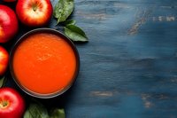 Fresh red apples and homemade tomato gazpacho soup in black bowl on dark blue rustic wooden background with green leaves and copy space.