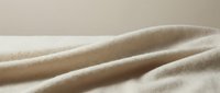 Soft beige fabric with gentle folds and waves creating elegant textile texture for fashion design and interior decoration projects.