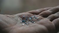 Small blue and clear glass beads scattered in open palm of hand, crafting supplies for jewelry making and creative projects.