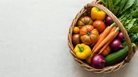 Fresh organic vegetables in wicker basket including tomatoes, carrots, peppers and leafy greens on neutral background for healthy cooking and nutrition.
