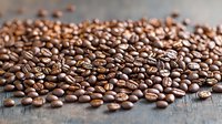 Fresh roasted coffee beans scattered on rustic wooden surface with selective focus, showing rich brown color and natural texture for cafe and food industry use.