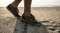 Male runner in dark athletic shoes jogging along sandy beach shoreline at sunrise or sunset, fitness and outdoor exercise concept for wellness and active lifestyle.