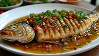 Whole steamed fish with soy sauce, ginger and scallions on white plate. Traditional Asian cuisine dish with savory brown sauce and fresh herbs garnish.