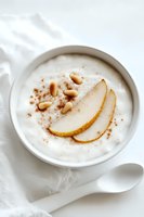 Creamy white yogurt bowl topped with fresh pear slices, pine nuts and cinnamon powder, served with ceramic spoon on light background. Healthy breakfast concept.