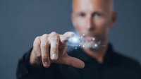 Businessman interacting with futuristic digital hologram, demonstrating innovative technology with glowing particles floating above his fingertips against dark background.