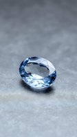 Blue faceted gemstone with brilliant cut reflecting light on gray textured surface for jewelry design and luxury product photography.