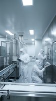 Pharmaceutical workers in sterile cleanroom environment operating manufacturing equipment with stainless steel tanks and control panels for drug production.