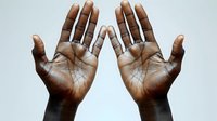 Open dark-skinned palms showing life lines and skin texture details against light background, symmetrical composition displaying both hands raised in surrender gesture.