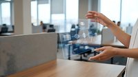 Woman with medium skin tone in business casual attire gesturing at digital holographic interface displaying data visualization in modern office workspace for technology and innovation concepts.