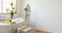 Human skeleton relaxing in modern bathroom bathtub with towel on head, spa day concept for anatomy education, medical humor and wellness lifestyle.
