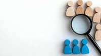 Wooden and blue figures with magnifying glass on white background, representing human resources, recruitment and talent search concept for business.
