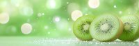 Fresh kiwi fruit slices arranged in row on sparkling surface against soft green bokeh background, creating refreshing summer mood for food and health concepts.