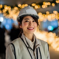 Smiling Asian female engineer wearing white hard hat and safety uniform with warm bokeh lights in industrial construction site background.