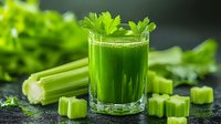 Fresh green celery smoothie in glass with raw celery stalks and cut pieces on dark background, healthy detox juice drink garnished with parsley leaf.