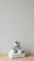 Ceramic sheep figurine standing atop stacked white gift boxes with silver ribbons on wooden surface against neutral background, suitable for holiday retail and festive marketing campaigns.