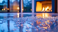 Cozy fireplace glowing warmly in modern living room with sparkling water droplets on wooden floor creating magical bokeh lights during evening hours.