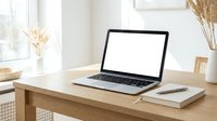 Laptop with blank screen on wooden desk in bright office workspace with notebook and dried flowers for mockup and design projects.
