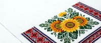 Traditional embroidered textile with bright sunflowers and folk geometric ornament in red, blue and green on white fabric background.
