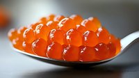 Fresh red caviar on silver spoon with soft focus background, macro shot showing glossy texture and translucent orange spheres of salmon roe.
