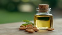Golden almond oil in glass bottle with cork stopper and fresh almonds on wooden surface for natural skincare and aromatherapy treatments.