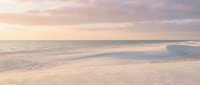 Serene beach scene with soft pink and purple sunset colors reflecting on wet sand and gentle ocean waves creating peaceful coastal atmosphere.