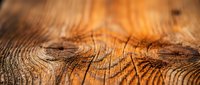 Macro shot of weathered wood grain texture with warm golden-brown tones and deep natural cracks, suitable for backgrounds, design elements, and woodworking projects.