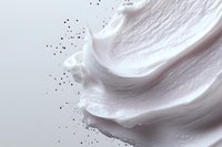 Smooth white cream texture with scattered black particles against light background, cosmetic product close-up showing luxurious skincare consistency.