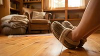 Cozy feet in warm knitted slippers relaxing on wooden floor in comfortable living room with soft natural lighting and home interior decor.