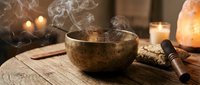 Tibetan singing bowl with smoking incense creates peaceful meditation atmosphere with warm candles and salt lamp on wooden table for wellness rituals.