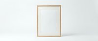 Empty wooden frame with white mat standing against light gray wall, minimalist home decor mockup for artwork display and interior design projects.
