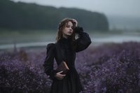Young woman in black dress standing in purple lavender field on moody overcast day with misty mountains in background for romantic portrait photography.