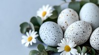 Speckled quail eggs with fresh daisies and eucalyptus leaves arranged on light background, creating natural spring composition for Easter celebration.