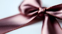 Elegant satin ribbon bow in dusty rose pink color with delicate texture and soft shadows against light background, macro close-up photography.