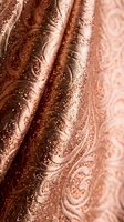 Luxurious copper metallic fabric with ornate paisley pattern and shimmering sequins creates elegant draped textile for fashion and interior design projects.