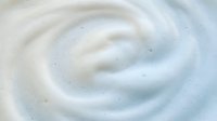 Creamy white swirl texture with smooth flowing curves and soft bubbles for skincare cosmetics and dairy product backgrounds.