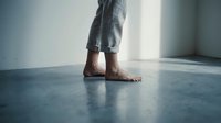 Barefoot person wearing rolled denim jeans standing on concrete floor in minimalist interior space with natural light, suitable for lifestyle and wellness content.
