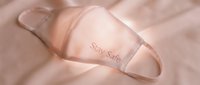 Soft pink fabric face mask with Stay Safe text resting on pastel cloth, symbolizing health protection and pandemic awareness.
