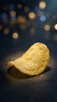 Golden crispy potato chip with salt crystals on dark surface with bokeh lights background for snack food advertising and culinary content.