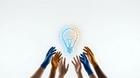 Diverse hands reaching toward glowing lightbulb symbolizing teamwork, innovation and creative collaboration in business brainstorming sessions.
