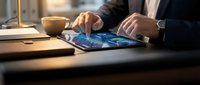 Professional businessman using digital tablet with global network interface at modern office desk with coffee cup and warm lighting.