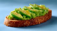 Fresh sliced avocado on toasted sourdough bread garnished with black pepper and sea salt, served on blue background, macro food photography.