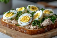 Fresh hard-boiled egg sandwich with tuna spread, parsley and black pepper on rustic whole grain bread, served on wooden cutting board. Close up food photography.