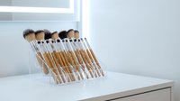 Professional makeup brush set with natural bristles organized in clear acrylic holder on white vanity table for beauty routine and cosmetic application.