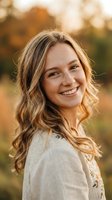 Happy young blonde woman smiling warmly in golden hour light wearing casual sweater outdoors in autumn park setting for lifestyle photography.