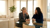 Two professional businesswomen having friendly conversation in modern office meeting room with large windows and natural light for corporate communication.
