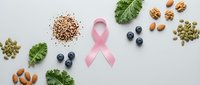 Pink ribbon surrounded by healthy superfoods including nuts, seeds, berries and leafy greens on white background for breast cancer awareness campaign.