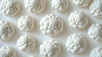 Fresh organic cauliflower florets arranged in rows on white background, top view. Clean minimalist food pattern showing natural vegetable texture.